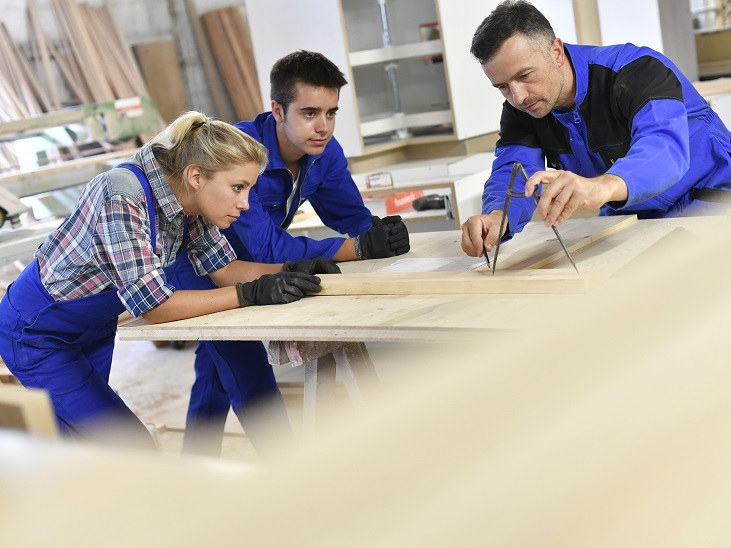 Munkásruhába öltözött emberek méricskélnek egy munkaasztal körül