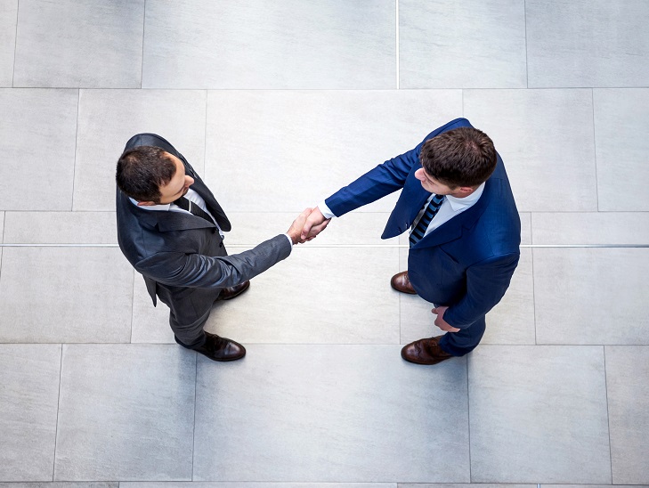 Két fiatal öltönyös férfi kezet fog egymással